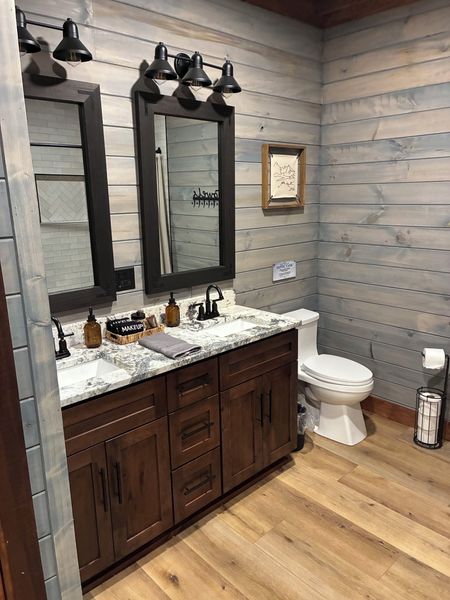 Double vanity with dark wood cabinets, a granite top, and two black framed mirrors against plank walls