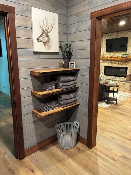 Floating wood shelves stacked with towels, with the living room fireplace seen through the doorway
