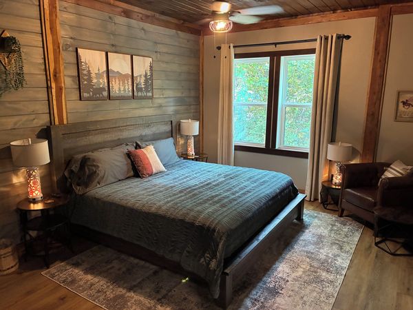 Barnhouse bedroom with a king bed, bedding, a wood-plank accent wall, and a sitting chair by the window