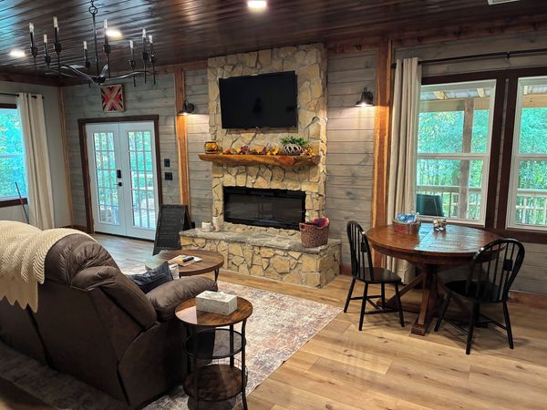 Round dining table by the windows, with the stone fireplace, French doors, and a recliner nearby
