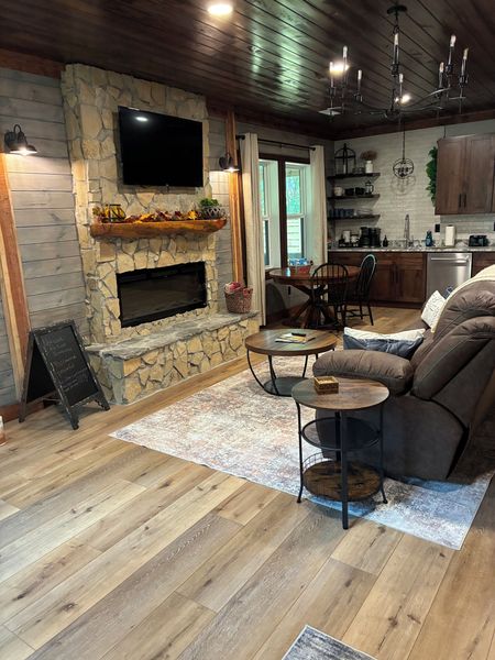 Stone fireplace with an electric insert and TV, a recliner sofa, and the kitchen beyond