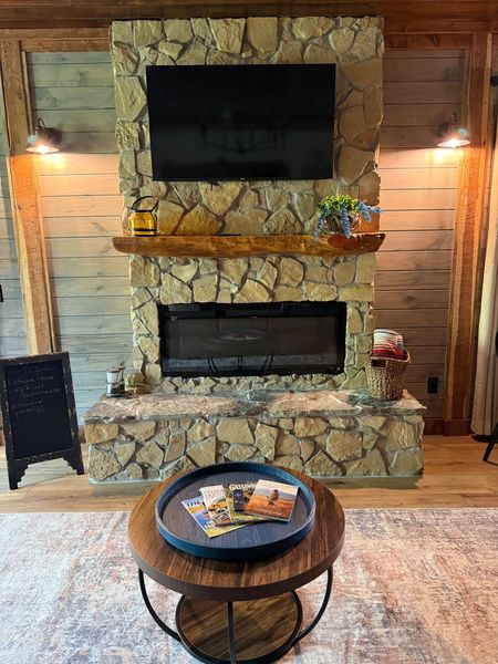 Stone fireplace with a wall-mounted TV and wood mantel, and a round coffee table in front