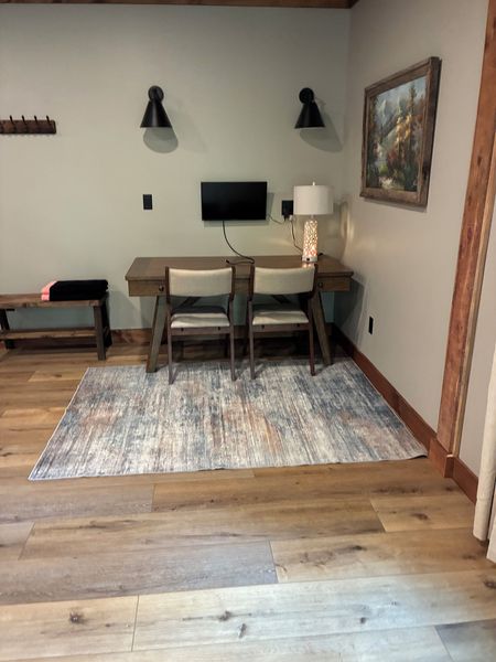Desk with two chairs, a wall-mounted screen, and two wall lamps on a rug