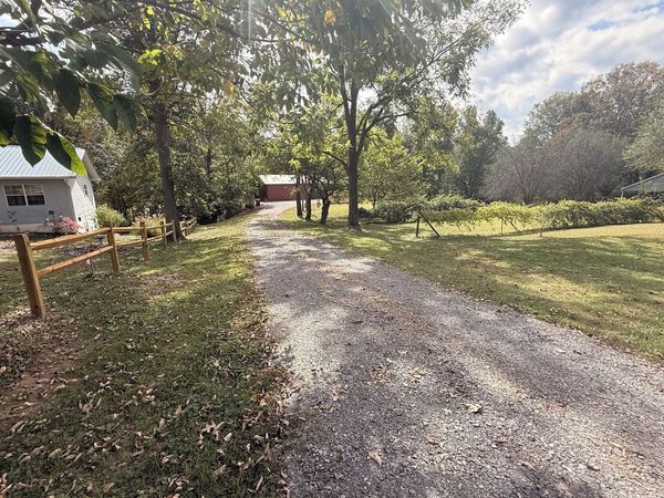 Gravel driveway with a split-rail fence leading to the red barn in the distance