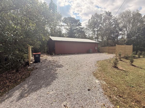 Gravel parking area leading to the red barn, with a wooden privacy fence