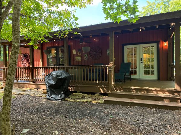 Front of the red Barnhouse with its covered porch and French doors, seen from the yard under the trees