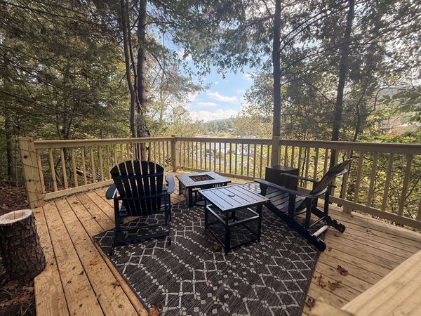 Overlook deck with Adirondack chairs, a fire table, and an outdoor rug among the trees