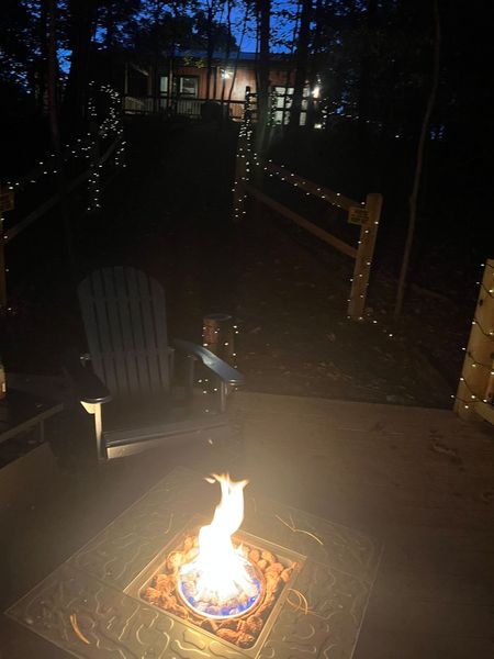 Fire table glowing at night on the deck, with string lights along the path and the lit Barnhouse beyond