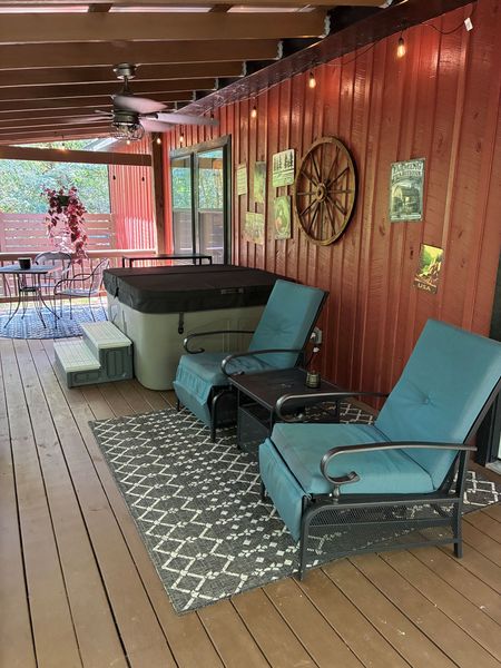 Covered porch with cushioned lounge chairs, an outdoor rug, and the hot tub against barn siding