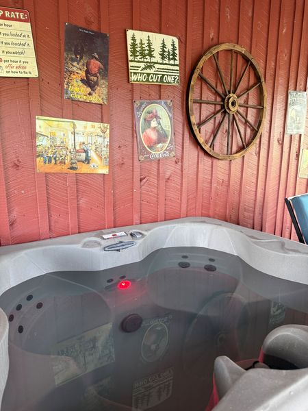 Hot tub under the covered porch, with a wagon wheel and vintage signs on the red wall