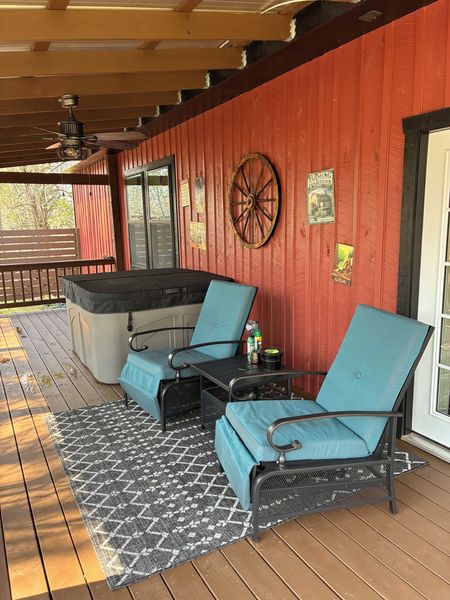 Covered front porch with two cushioned lounge chairs, an outdoor rug, and the covered hot tub against barn siding