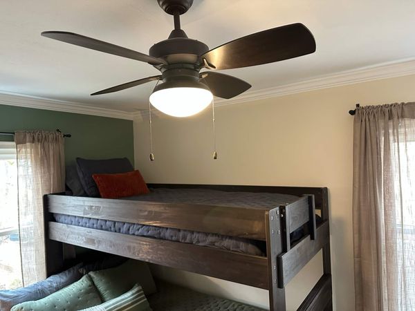 Dark wood bunk bed seen from the doorway, with the top bunk under a ceiling fan