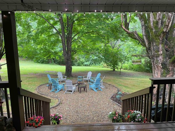 View from the covered porch steps to the fire pit circle and Adirondack chairs under big trees