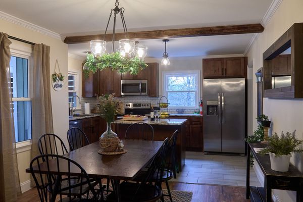 Dining table with black spindle chairs under a chandelier, open to the kitchen