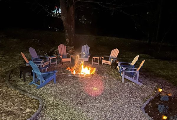 Fire pit burning at night, circled by Adirondack chairs