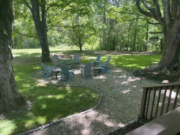 Fire pit circle and Adirondack chairs in the shade of big trees, seen from the deck