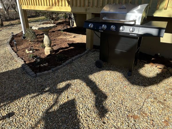 Stainless propane grill on the gravel beside the deck
