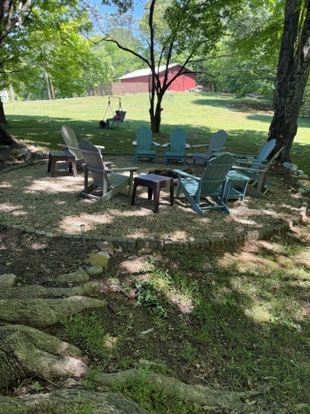 Fire pit circle with Adirondack chairs, and a red barn across the lawn in the distance