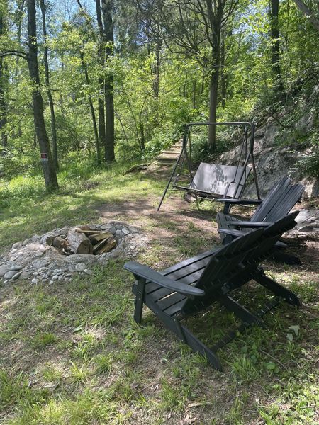 Riverside fire ring with dark Adirondack chairs and a wooden swing under the trees