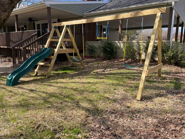 Wooden swing set with a green slide and swings in front of the covered deck