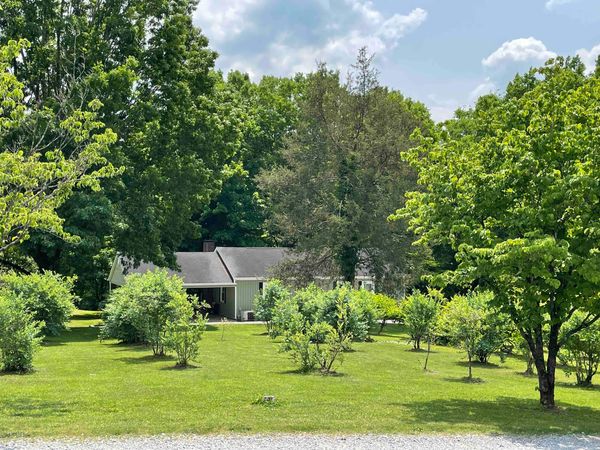 The Farmhouse across a wide green lawn planted with rows of young fruit trees and bushes