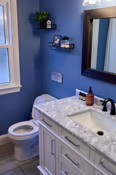 Guest bath vanity with a marble-look top beside the toilet and a window