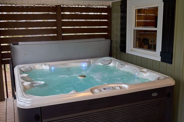 Hot tub with lit water on the covered porch beside a wood privacy screen