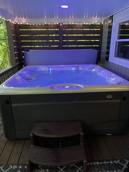 Hot tub glowing under the covered porch, with string lights and steps in front