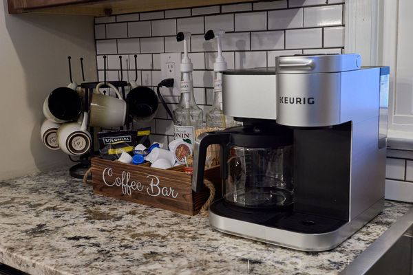 Coffee bar on a granite counter with a Keurig coffee maker, a mug rack, and a Coffee Bar box of pods