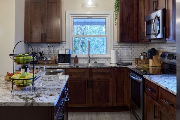 Kitchen sink under a window with dark wood cabinets, a subway-tile backsplash, and a stainless range and microwave