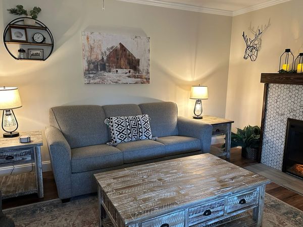 Living room with a sofa, a rustic coffee table, table lamps, and a barn painting on the wall