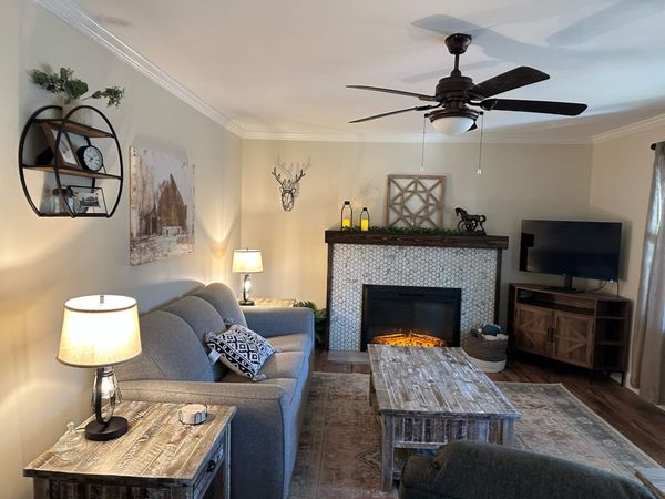 Living room with a ceiling fan, sofa, electric fireplace, TV on a wood console, and rustic coffee table
