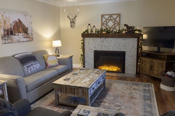 Living room with a sofa, an electric fireplace with a tile surround, a rustic coffee table, and a TV