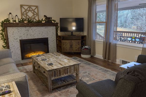 Electric fireplace with a tile surround and garland, a TV on a wood console, and a coffee table by the window