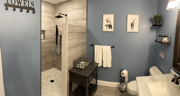 Master bathroom with a tiled walk-in shower, towel bar, and small wood side table
