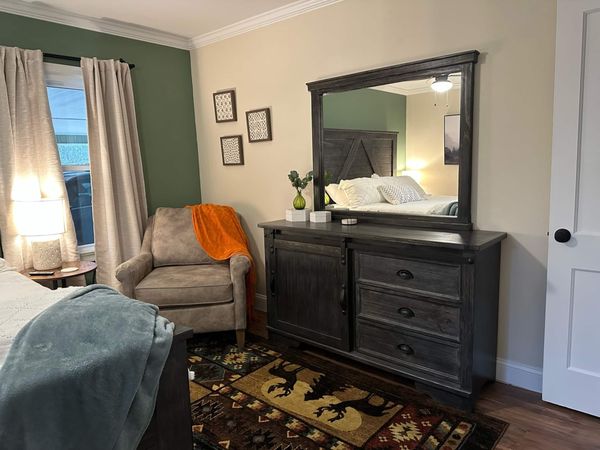 Master bedroom armchair beside a dark wood dresser with a large mirror