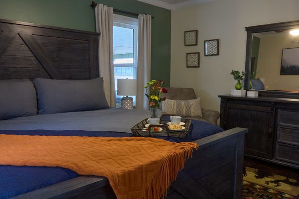 King bed with bedding, a throw, a breakfast tray, and a dresser with mirror behind