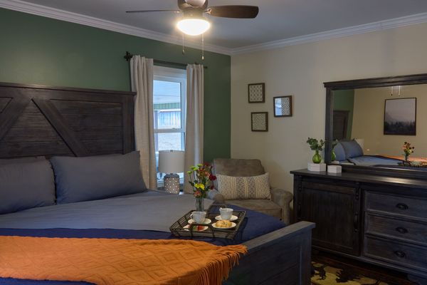 Master suite with a king bed, breakfast tray, armchair, and dresser with mirror under a ceiling fan