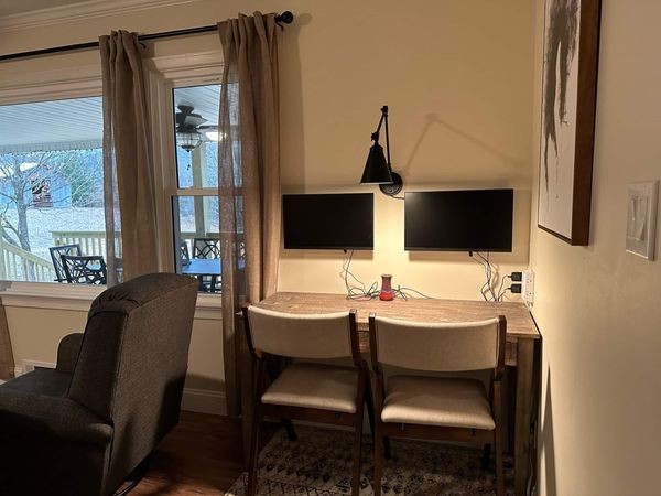 Work desk with two monitors and two chairs beside a window, with a recliner nearby