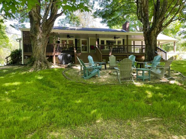 Back of the Farmhouse and its long covered deck across a sunny lawn, with Adirondack chairs around the fire pit