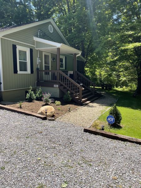 Side entrance of the Farmhouse with wooden steps, a small landscaped bed, and the gravel drive