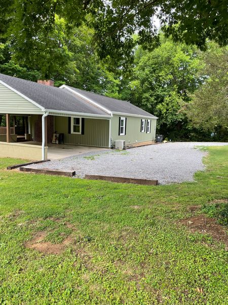 The Farmhouse and its gravel parking area beside the lawn, framed by tall trees