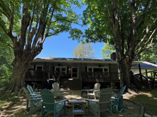 Adirondack chairs around the fire pit under two large trees, with the Farmhouse back deck behind