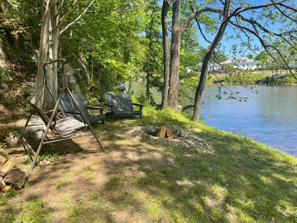 Porch swing and Adirondack chairs on the riverbank beside a fire ring, with the river alongside