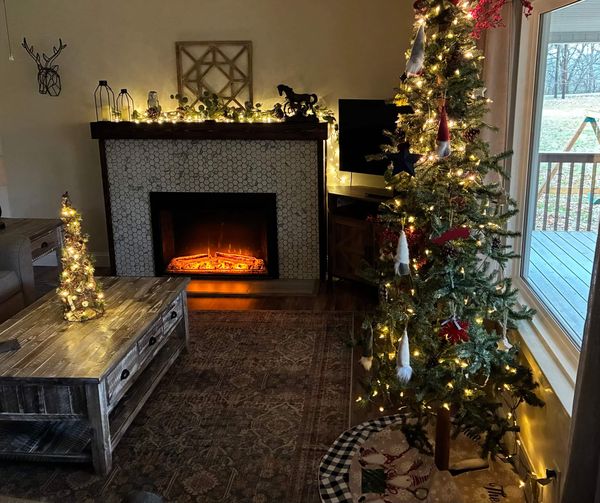 Living room decorated for Christmas with a lit tree beside the electric fireplace