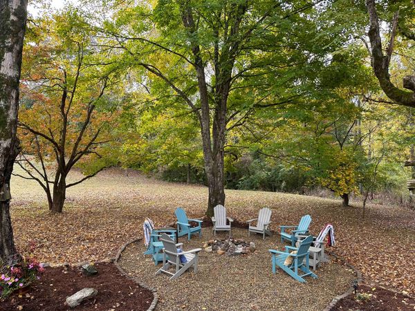 Fire pit circle with Adirondack chairs among fall foliage and fallen leaves