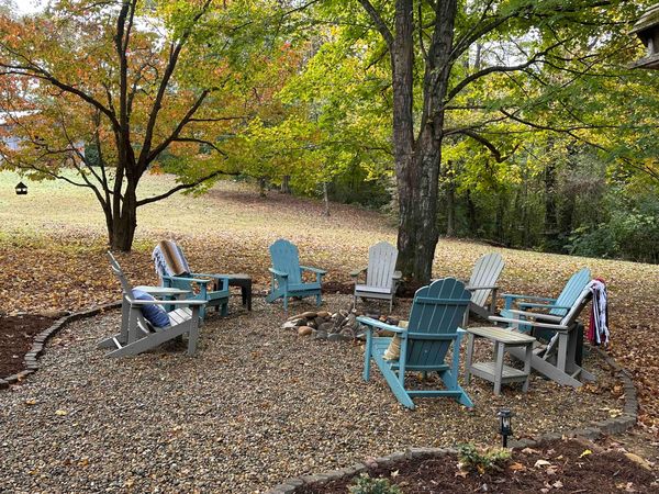 Adirondack chairs around the fire pit with orange and yellow fall leaves overhead